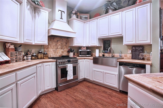 kitchen with stainless steel appliances, a sink, white cabinetry, light wood-style floors, and custom range hood