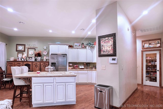 kitchen with a kitchen island, visible vents, white cabinets, light countertops, and stainless steel fridge