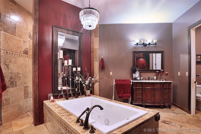 bathroom featuring stone tile floors, toilet, an inviting chandelier, vanity, and a jetted tub