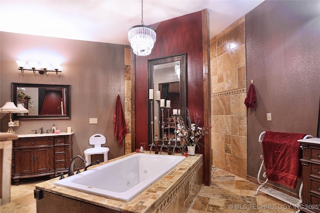 full bath with an inviting chandelier, a tub with jets, stone tile flooring, and vanity