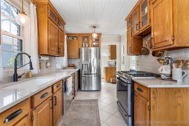 kitchen with light tile patterned flooring, a sink, hanging light fixtures, appliances with stainless steel finishes, and brown cabinetry