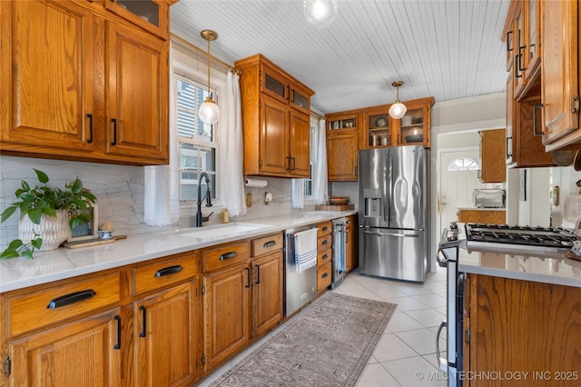 kitchen featuring pendant lighting, brown cabinets, light tile patterned floors, appliances with stainless steel finishes, and a sink