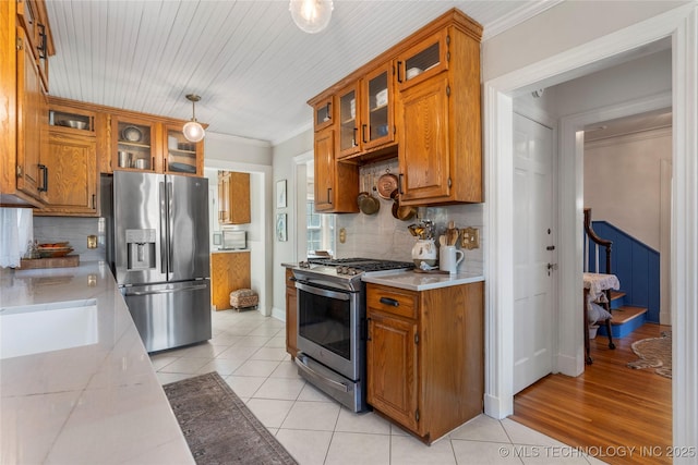 kitchen featuring light tile patterned floors, appliances with stainless steel finishes, brown cabinets, light countertops, and crown molding