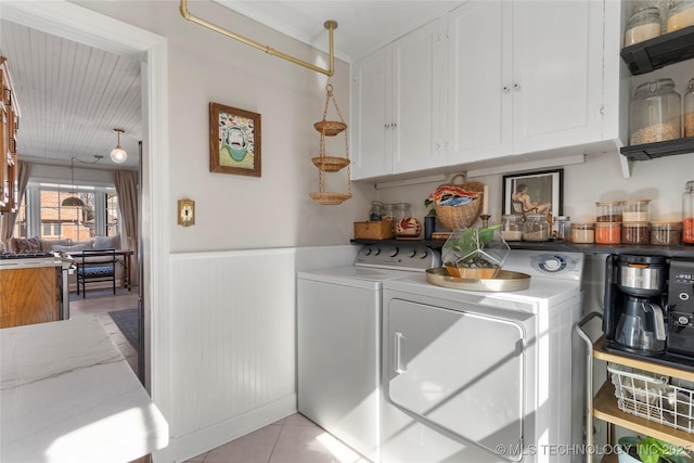 laundry area featuring light tile patterned flooring, wainscoting, washing machine and dryer, and cabinet space