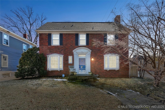 colonial home with brick siding, fence, roof with shingles, a chimney, and a front yard