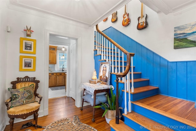 stairs with wood finished floors and crown molding