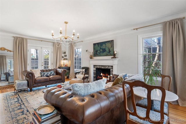 living area featuring ornamental molding, wood finished floors, french doors, a fireplace, and a notable chandelier