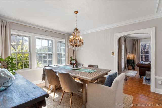 dining space with arched walkways, ornamental molding, light wood-style floors, a chandelier, and baseboards