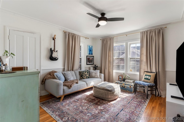 living area with crown molding, a ceiling fan, and wood finished floors