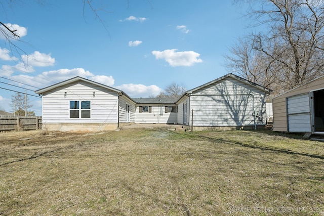 rear view of property featuring a storage unit, fence, a lawn, and an outbuilding