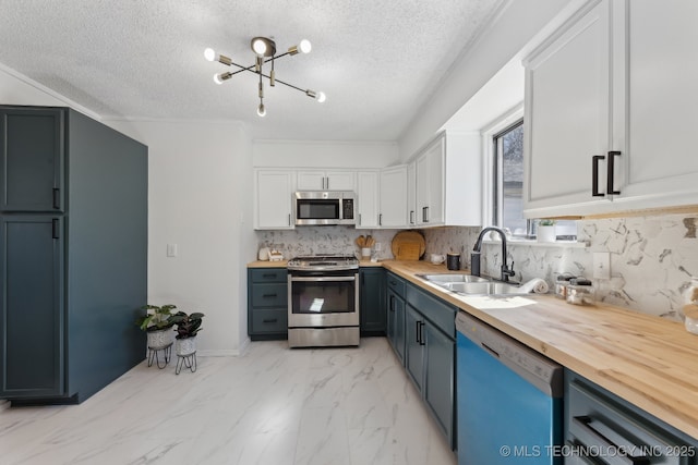 kitchen featuring marble finish floor, stainless steel appliances, butcher block counters, white cabinets, and a sink