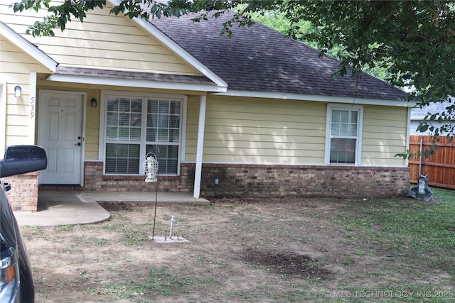 exterior space with roof with shingles, fence, a patio, and brick siding