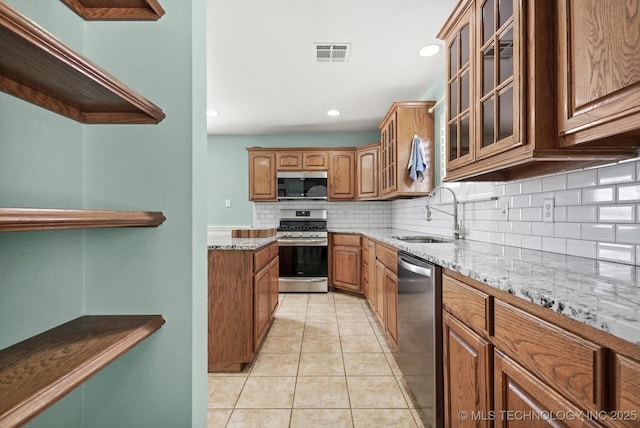 kitchen featuring visible vents, brown cabinetry, light stone countertops, stainless steel appliances, and a sink