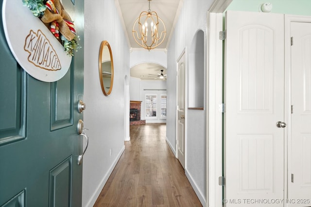 foyer featuring arched walkways, ceiling fan with notable chandelier, dark wood-type flooring, a fireplace, and baseboards