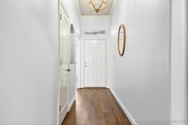 hall with visible vents, dark wood finished floors, baseboards, ornamental molding, and a chandelier