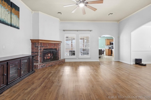 unfurnished living room featuring ceiling fan, a brick fireplace, crown molding, and wood finished floors