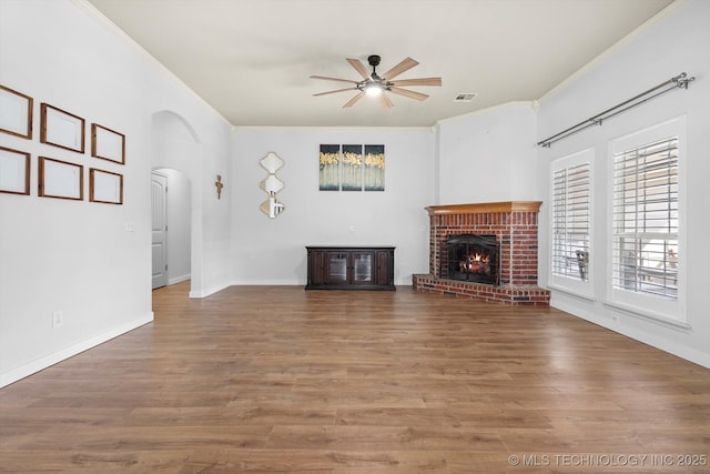 unfurnished living room with arched walkways, wood finished floors, and ornamental molding