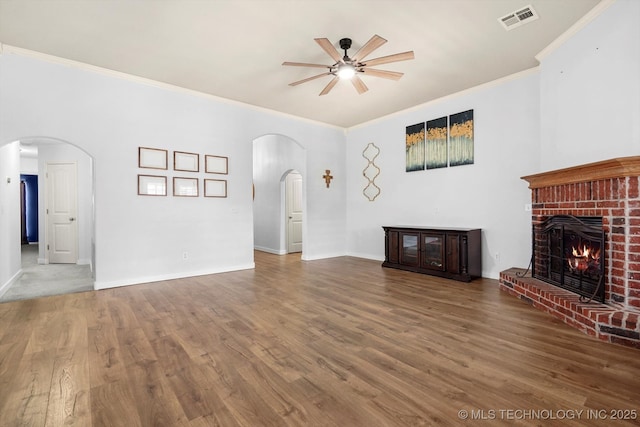 unfurnished living room featuring baseboards, visible vents, arched walkways, wood finished floors, and a fireplace