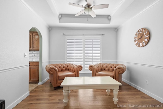 living area featuring ornamental molding, a tray ceiling, ceiling fan, and light wood finished floors