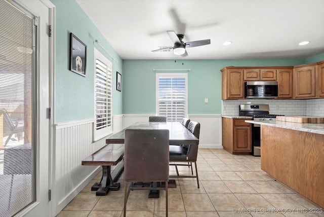 kitchen with brown cabinets, light tile patterned floors, tasteful backsplash, appliances with stainless steel finishes, and wainscoting