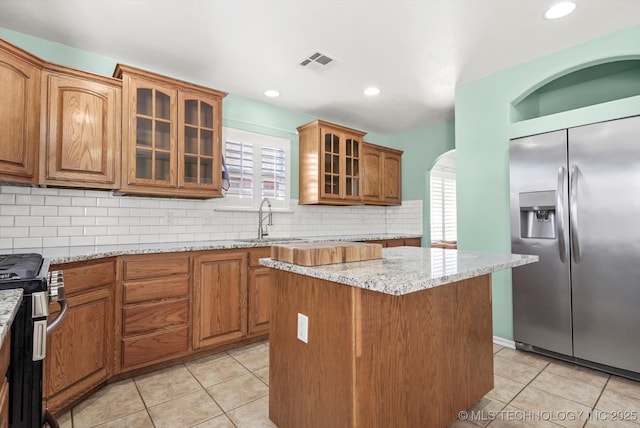 kitchen with visible vents, electric range oven, stainless steel fridge with ice dispenser, brown cabinets, and light stone countertops