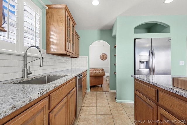 kitchen with appliances with stainless steel finishes, brown cabinetry, a sink, and backsplash