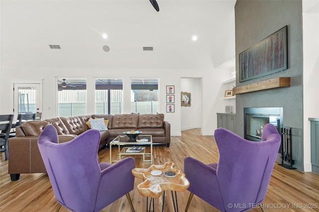 living area with a large fireplace, light wood-style flooring, and visible vents