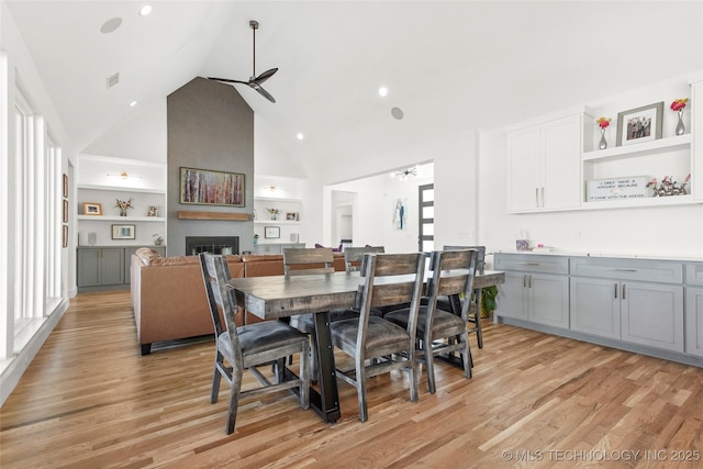 dining room with built in features, a fireplace, light wood finished floors, visible vents, and a ceiling fan