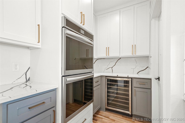 kitchen featuring beverage cooler, white cabinets, light stone counters, light wood-type flooring, and double oven