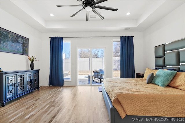 bedroom with a tray ceiling, light wood-type flooring, recessed lighting, and access to exterior