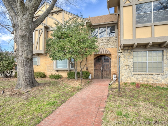 entrance to property featuring stone siding, brick siding, roof with shingles, and stucco siding