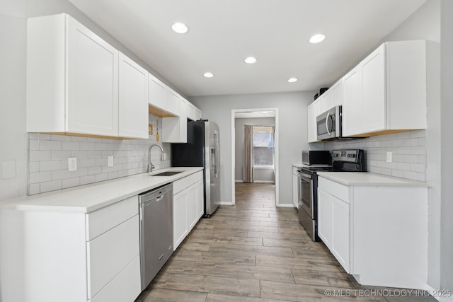 kitchen with appliances with stainless steel finishes, light countertops, light wood-type flooring, white cabinetry, and a sink