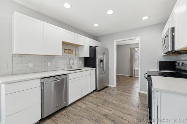 kitchen with a sink, white cabinetry, appliances with stainless steel finishes, light wood-type flooring, and decorative backsplash