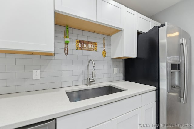 kitchen with appliances with stainless steel finishes, white cabinetry, a sink, and backsplash