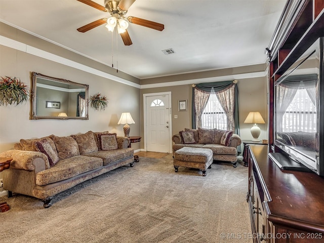 living area with visible vents, ornamental molding, carpet, and a ceiling fan