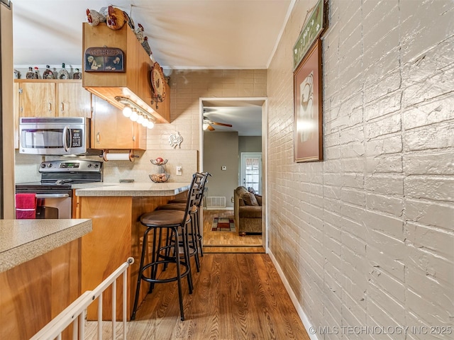 kitchen featuring visible vents, a ceiling fan, brick wall, dark wood-type flooring, and stainless steel appliances