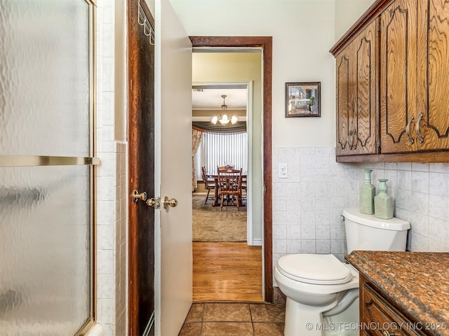 bathroom featuring a notable chandelier, tile walls, toilet, a shower with shower door, and tile patterned flooring