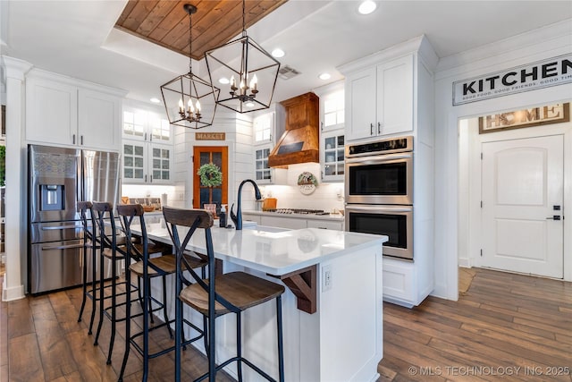 kitchen with a kitchen island with sink, stainless steel appliances, dark wood-type flooring, white cabinets, and glass insert cabinets