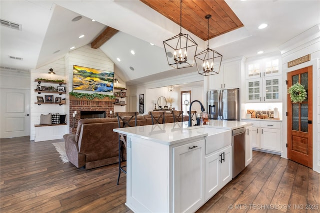 kitchen with lofted ceiling with beams, stainless steel appliances, dark wood-type flooring, visible vents, and a brick fireplace