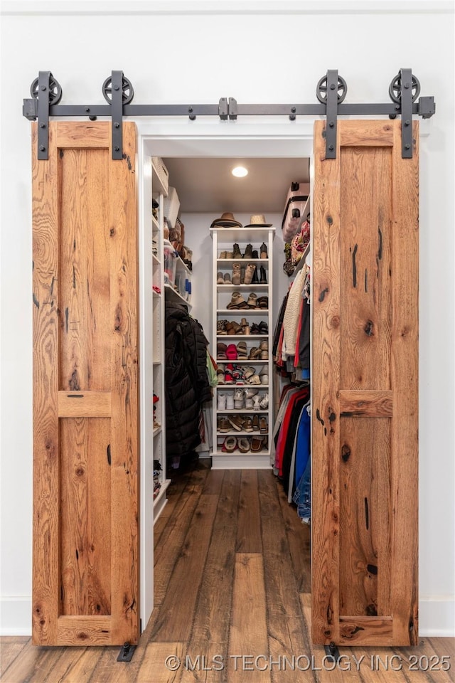 walk in closet with wood finished floors and a barn door