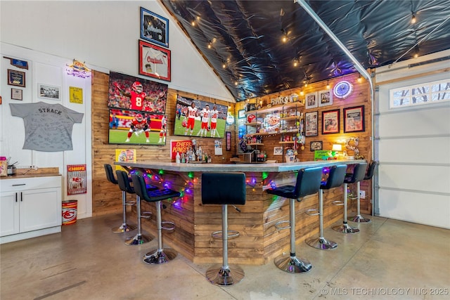 bar featuring concrete flooring, a bar, wood walls, and lofted ceiling