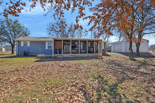 rear view of house featuring a garage, a sunroom, cooling unit, and an outbuilding