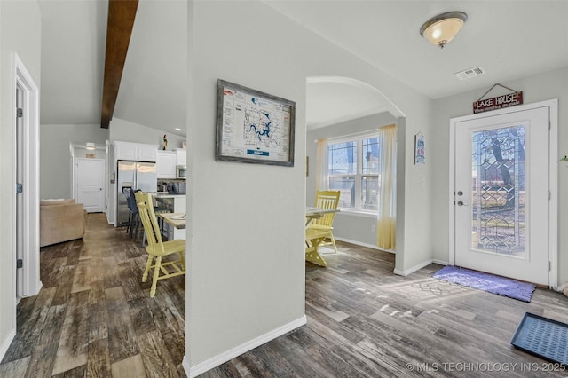 foyer with baseboards, visible vents, arched walkways, dark wood-style floors, and vaulted ceiling with beams