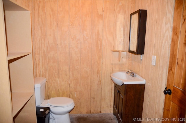 half bath with toilet, wood walls, and vanity