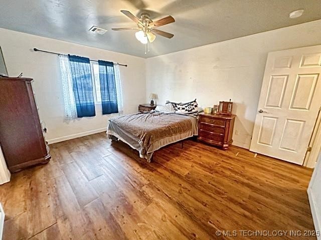 bedroom with a ceiling fan, baseboards, visible vents, and wood finished floors