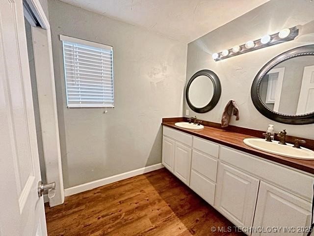 bathroom featuring double vanity, wood finished floors, a sink, and baseboards