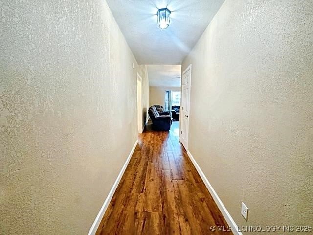 corridor featuring a textured wall, wood finished floors, and baseboards