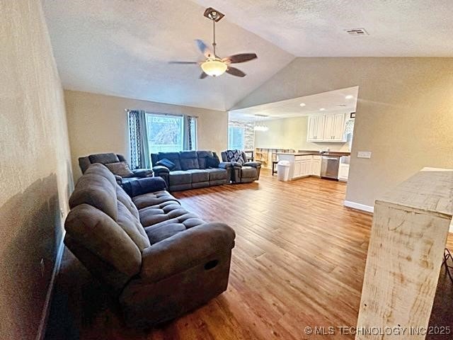 living room featuring a textured ceiling, light wood-style flooring, visible vents, a ceiling fan, and vaulted ceiling