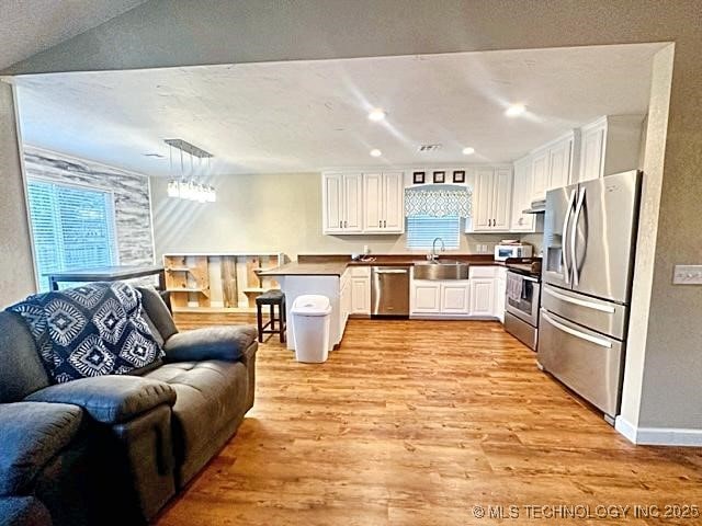 kitchen with light wood finished floors, appliances with stainless steel finishes, open floor plan, a peninsula, and a sink