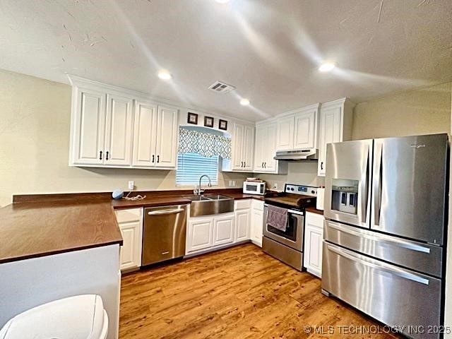 kitchen featuring under cabinet range hood, a sink, visible vents, appliances with stainless steel finishes, and dark countertops